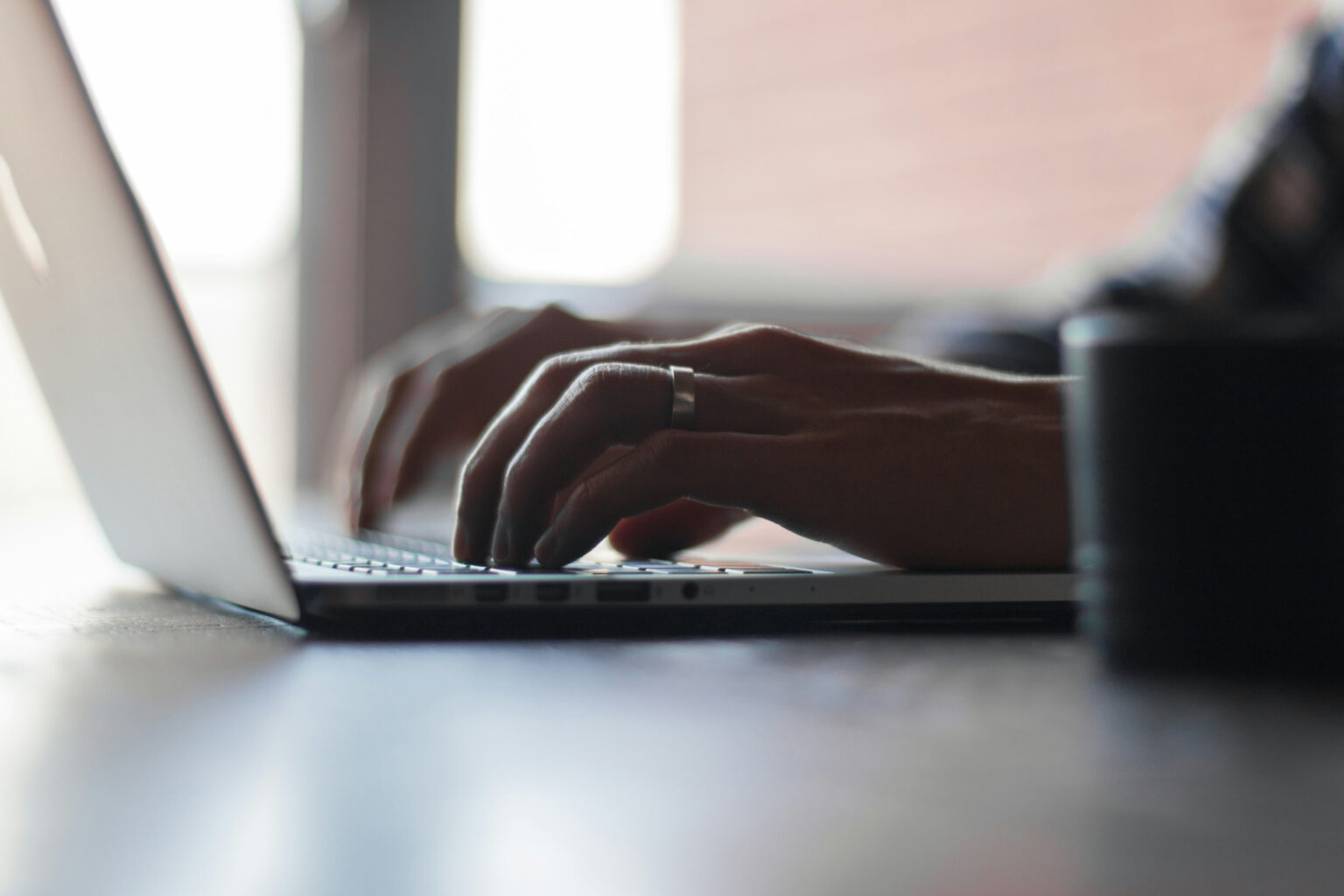 a close-up view of a woman's hands, wearing a wedding ring and using a laptop to pay a bill online